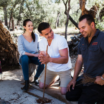 Two people learn traditional fire-making from an Aboriginal guide during a cultural tourism experience outdoors.